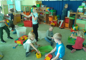 Grupa dzieci na dywanie bawi się klockami.